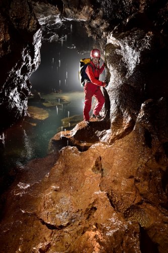 Akiyoshi-do (Akiyoshidai, Yamaguchi, Japon) - Spéléo progressant dans une petite galerie avec une petite cascatelle tombant du plafond (premier plan éclairé)(SP-19-0180)